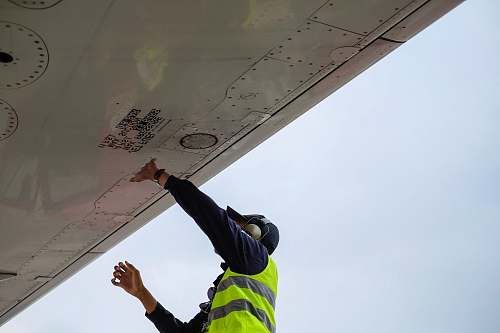 airplane wing man in green safety vest standing under white structure wing